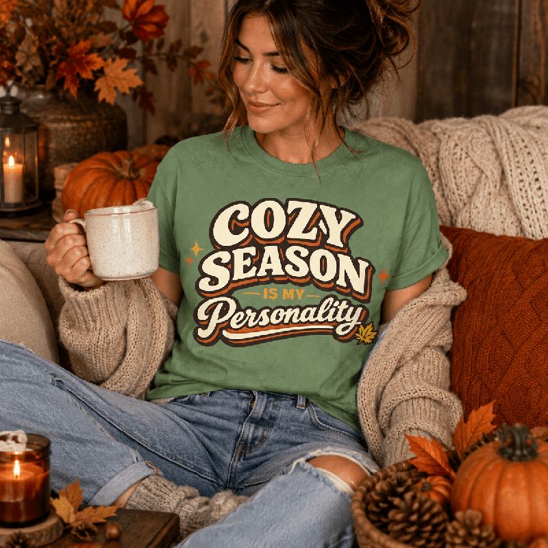 Woman sitting and holding a mug, wearing the Cozy Season Premium T-Shirt in leaf sage green