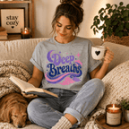 Woman sitting on a couch holding a mug and book, wearing the Deep Breaths Premium T-Shirt in athletic heather gray