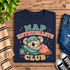 A folded mockup of Nap Enthusiasts Club cute animal graphic t-shirt in navy.