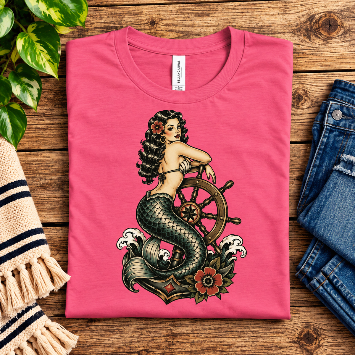 A folded mockup of Ship Wheel Mermaid vintage pinup graphic t-shirt in charity pink.