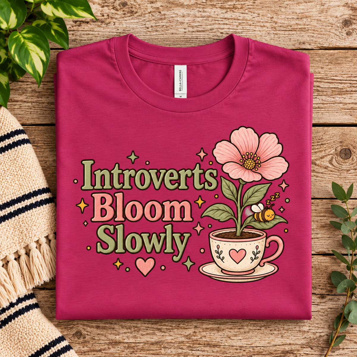 A folded mockup of Introverts Bloom Slowly cute plant graphic t-shirt in berry.