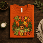 Happy Alone Premium T-Shirt in burnt orange, folded close-up styled with a candle and pinecones