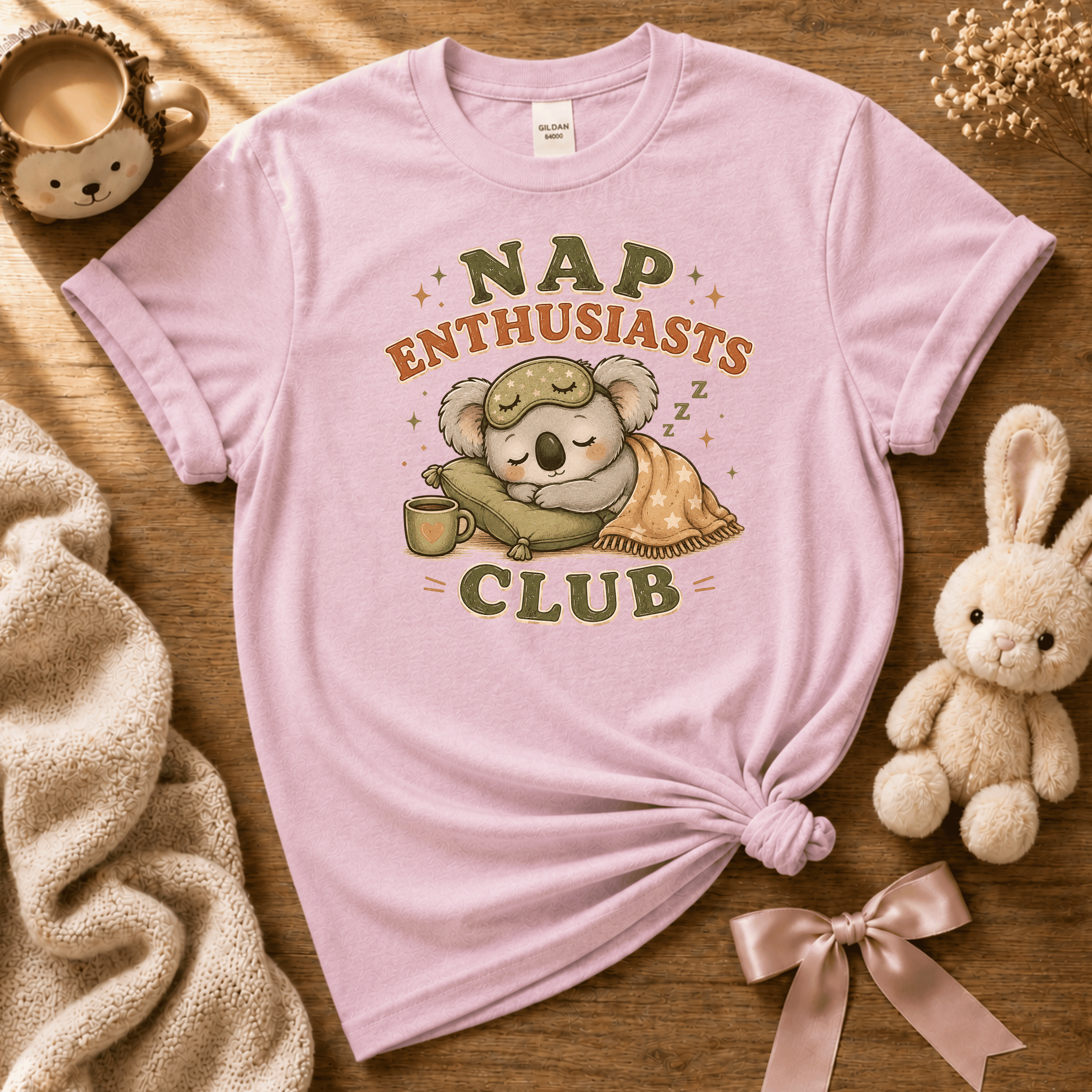 Nap Enthusiast Club cute animal graphic t-shirt displayed in a cozy flat lay in light pink.