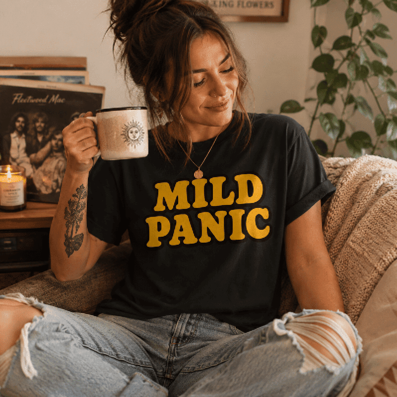 Woman holding a mug near vinyl records, wearing the Mild Panic Premium T-Shirt in vintage black