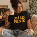Woman holding a mug near vinyl records, wearing the Mild Panic Premium T-Shirt in vintage black