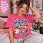 Woman sitting on a bed near neon wall art, wearing the Mono Mood Premium T-Shirt in charity pink