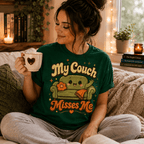 Woman sitting on a couch holding a mug, wearing the My Couch Misses Me Premium T-Shirt in evergreen