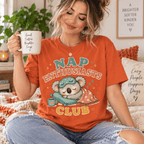 Woman holding a mug, wearing the Nap Enthusiasts Club Premium T-Shirt in burnt orange