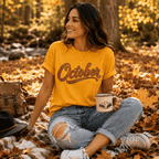 Woman sitting outdoors on fallen leaves, wearing the October Premium T-Shirt in gold