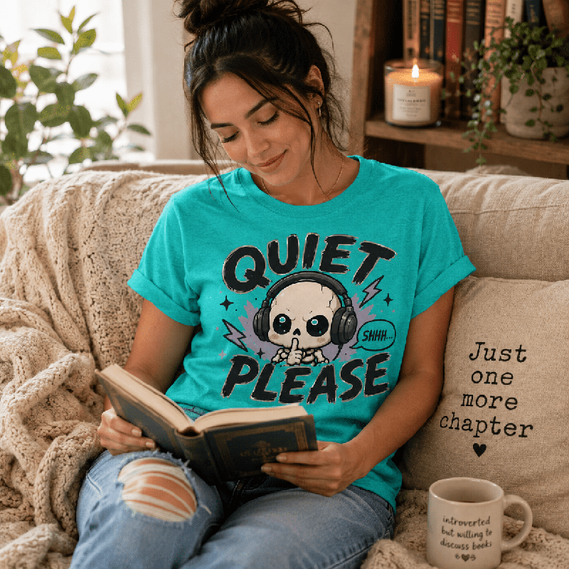 Woman reading a book on a couch, wearing the Quiet Please Premium T-Shirt in heather sea green