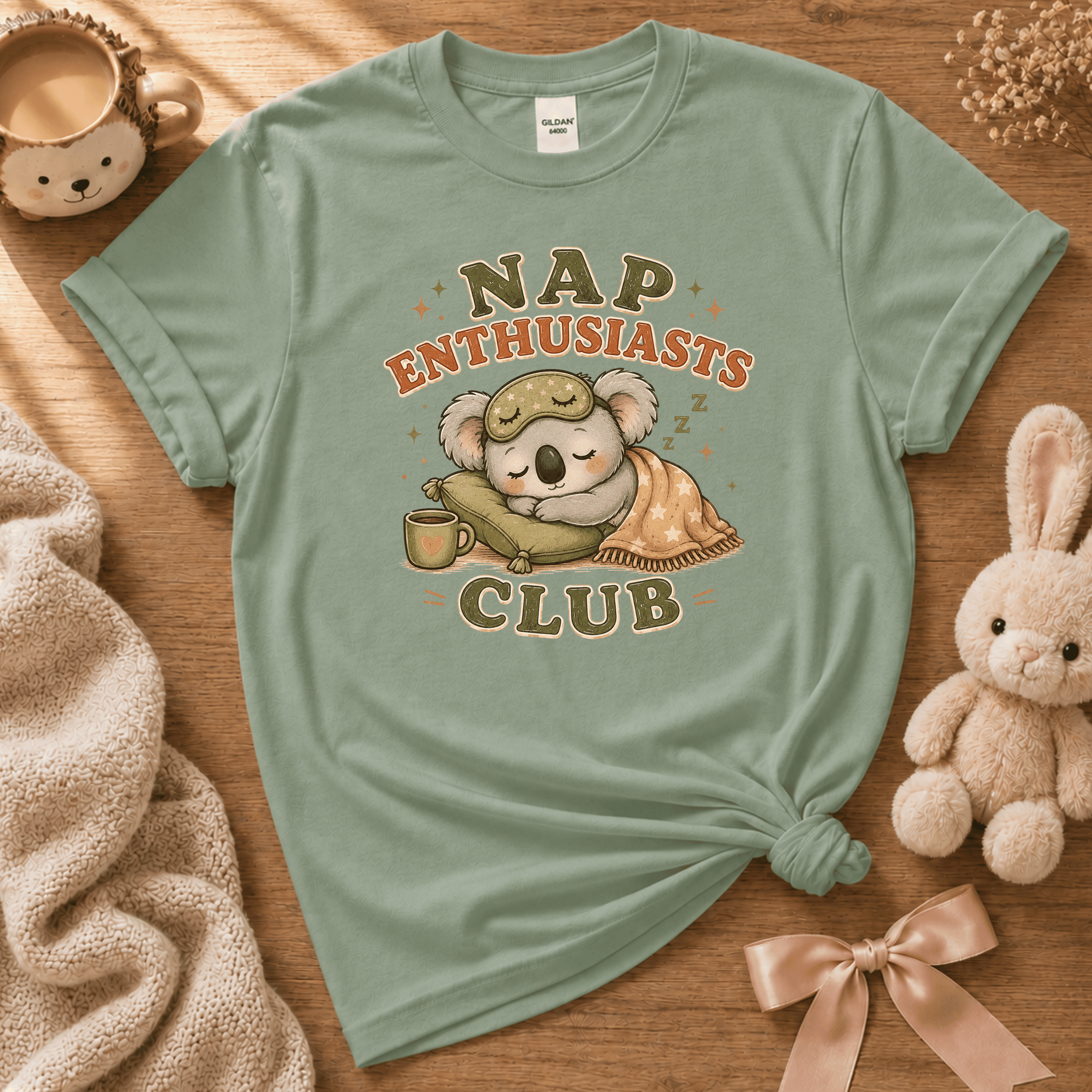 Nap Enthusiast Club cute animal graphic t-shirt displayed in a cozy flat lay in sage.
