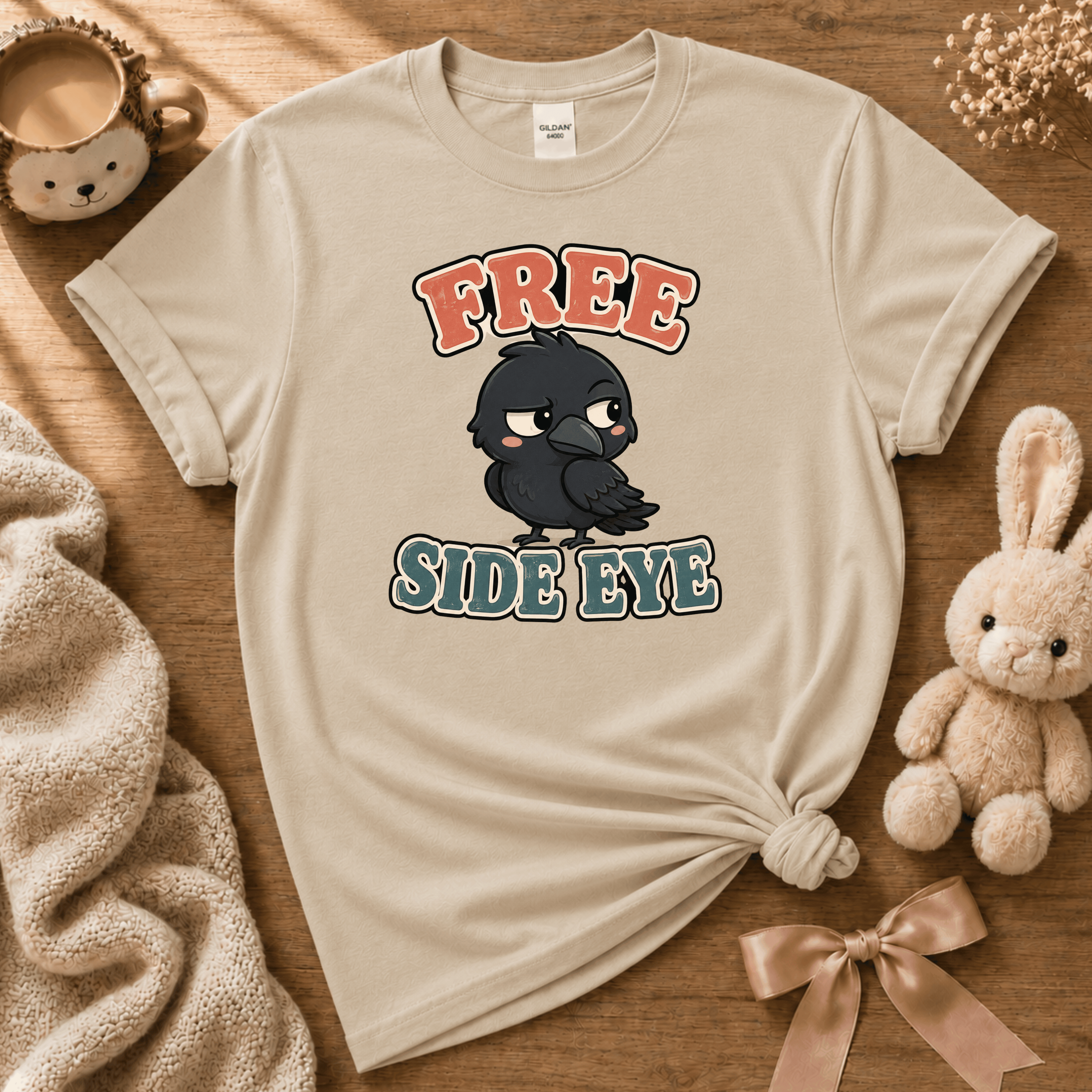 Free Side Eye cute animal graphic t-shirt displayed in a cozy flat lay in sand.