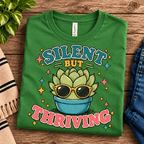 Silent But Thriving Premium T-Shirt in leaf green, folded close-up with neck tag showing
