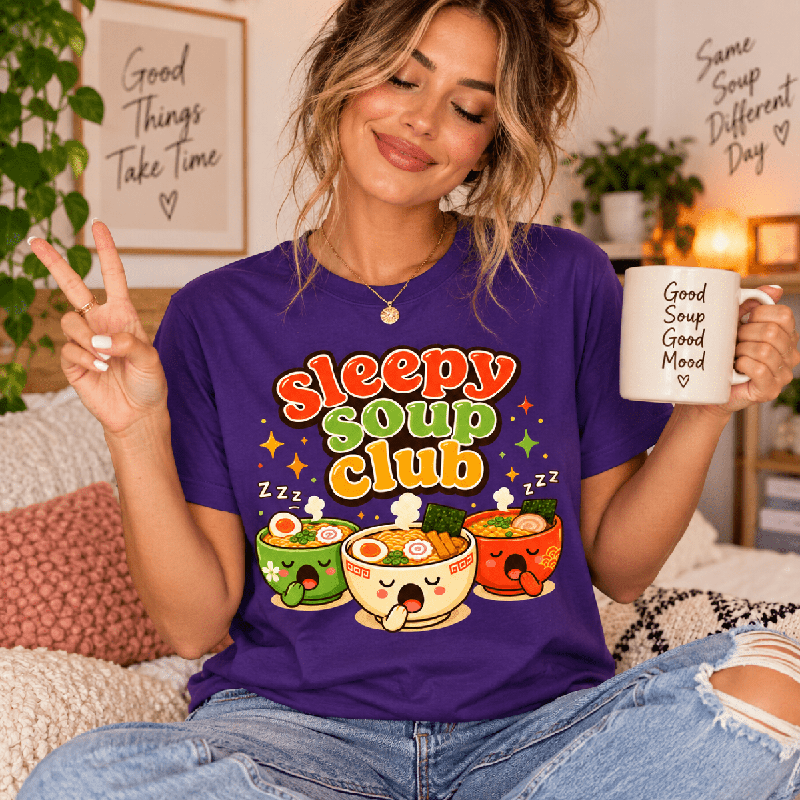 Woman holding a "Good Soup Good Mood" mug, wearing the Sleepy Soup Club Premium T-Shirt in team purple