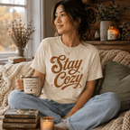 Woman holding a mug on a couch, wearing the Stay Cozy Premium T-Shirt in natural