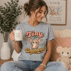 Woman holding a mug, wearing the Tiny But Unbothered Premium T-Shirt in athletic heather gray