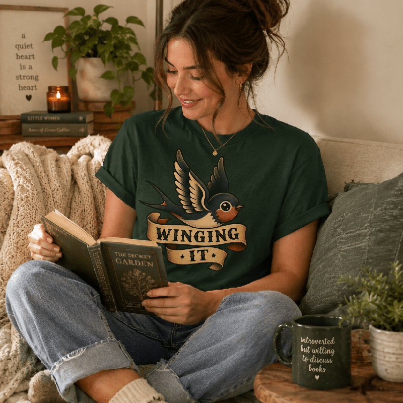 Woman reading a book on a couch, wearing the Winging It Premium T-Shirt in evergreen